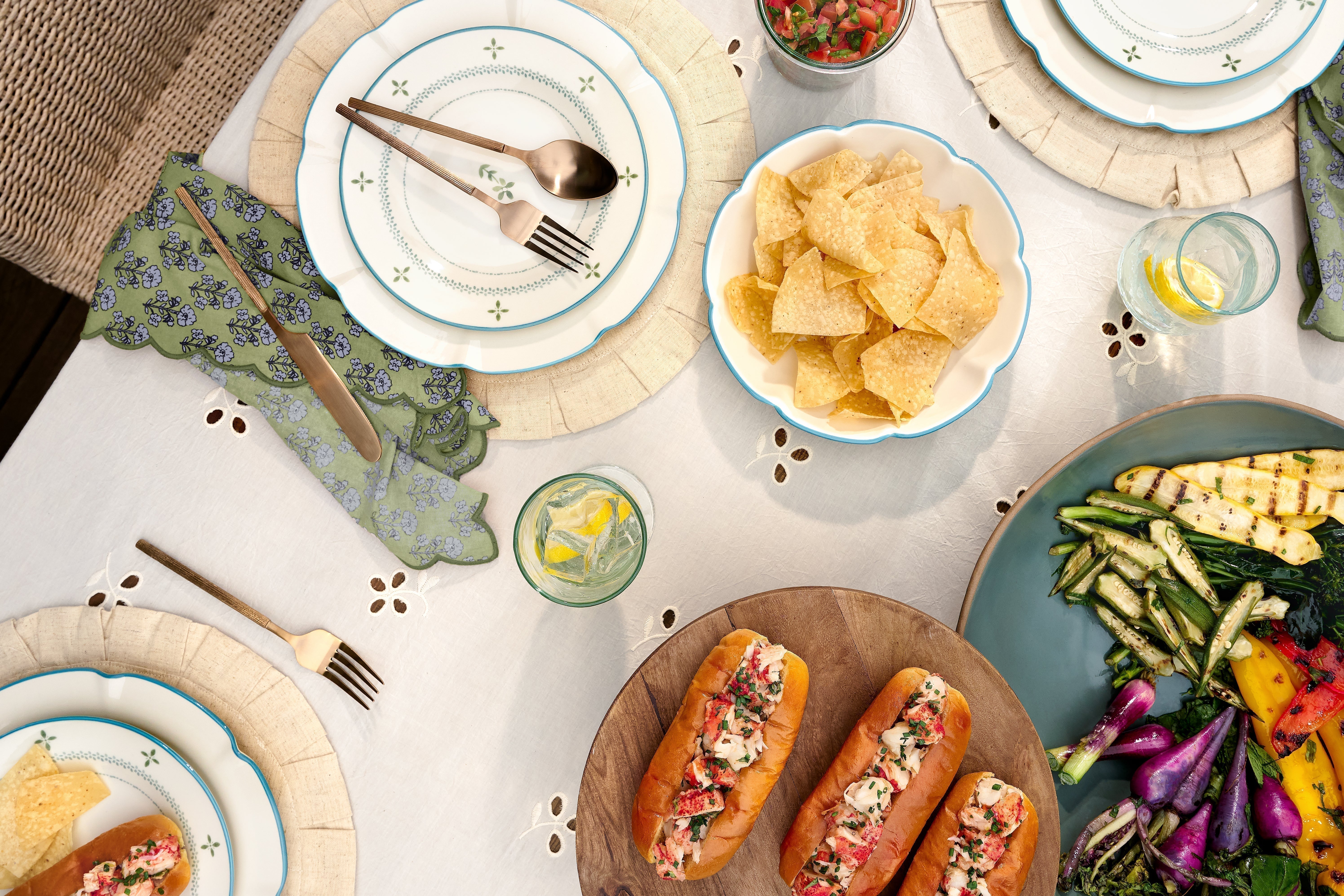 A summer tablescape featuring grilled vegetables, chips, sandwiches, and Magnoliass serveware at each place setting