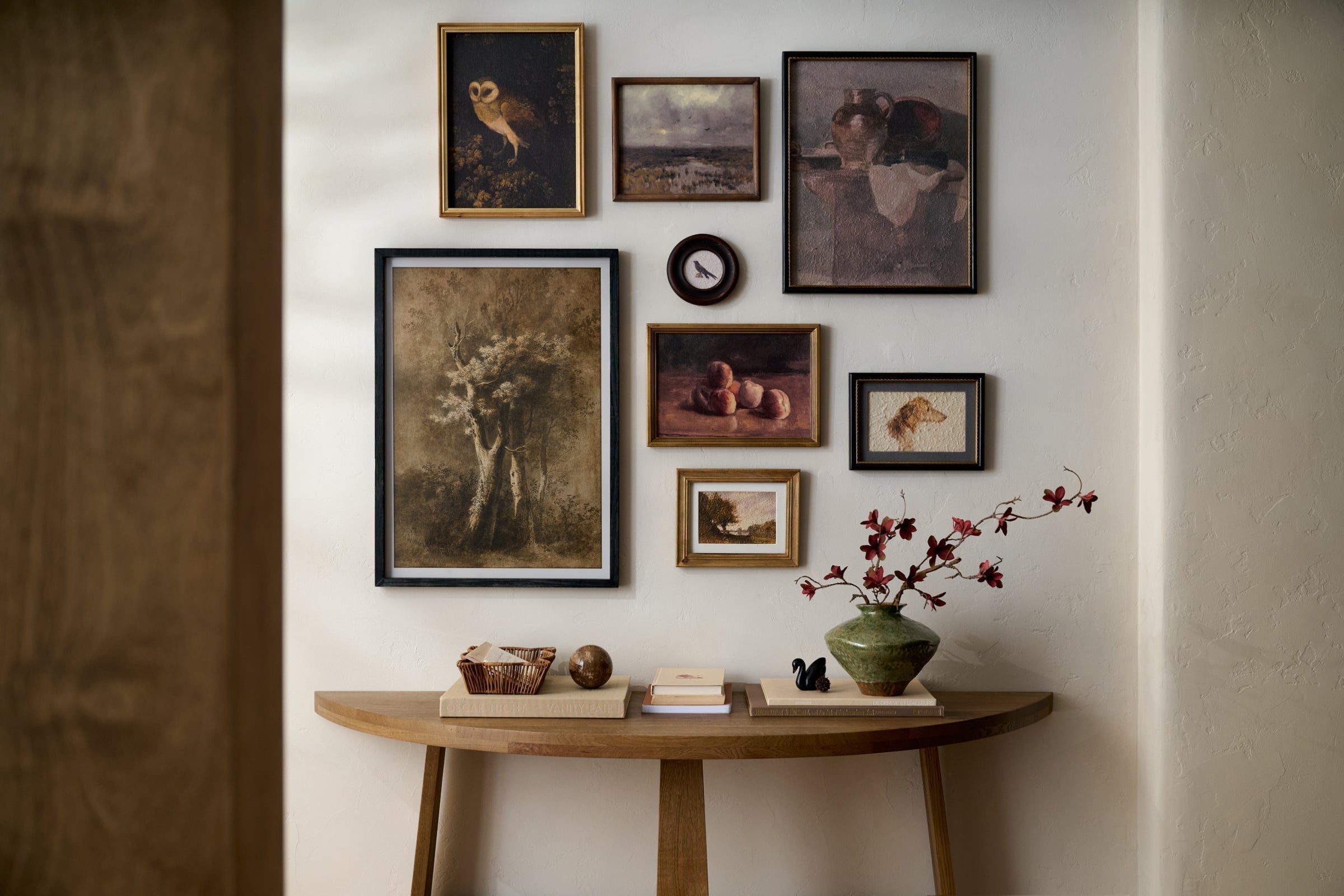 Gallery wall of framed art and wall decor above a console table with a green vase and maroon blossoms sticking out.