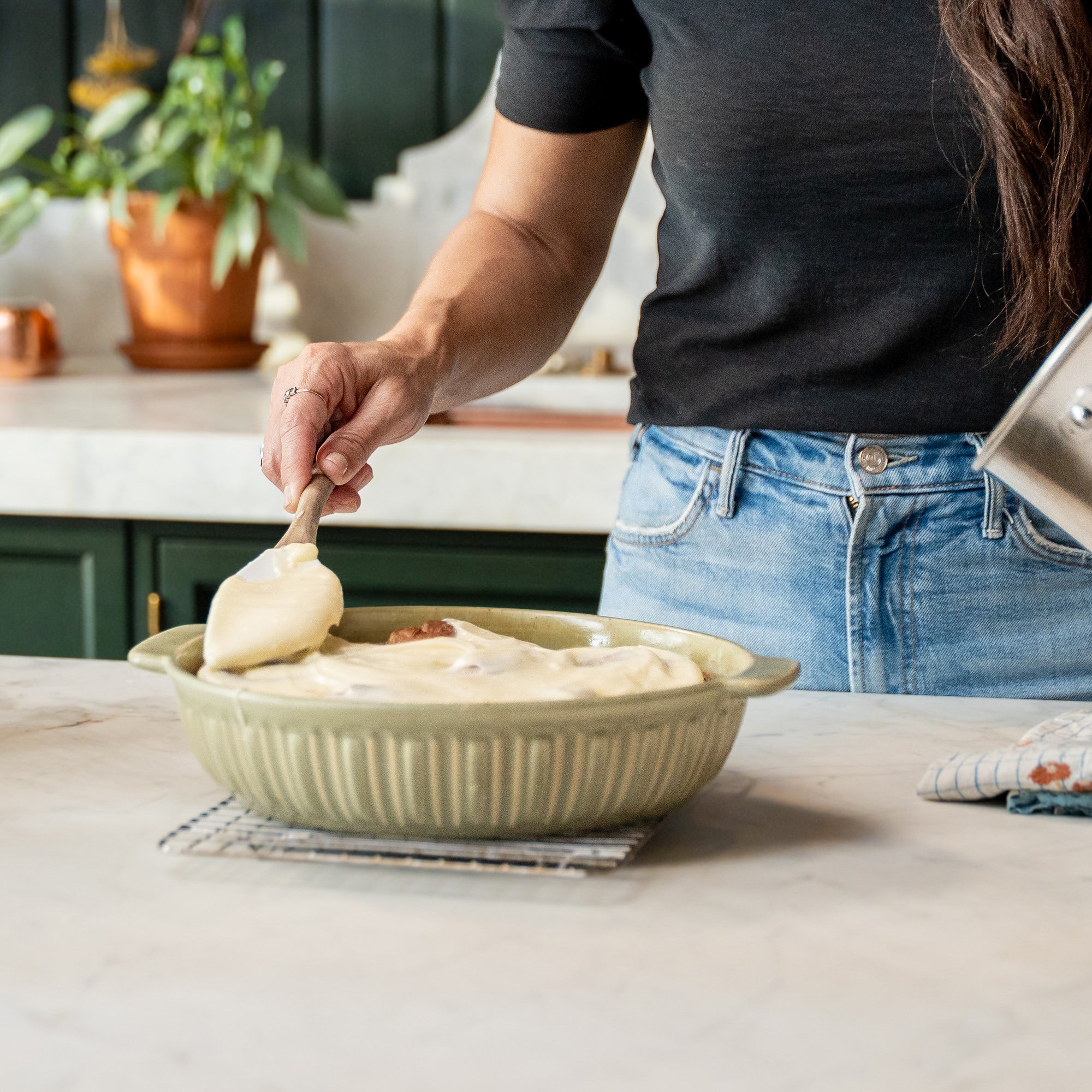 Joanna Gaines in her butler's pantry with a baking pan full of fresh cinnamon rolls.  She is standing at her kitchen island spreading the homemade cream cheese icing on the pan of fresh cinnamon rolls.