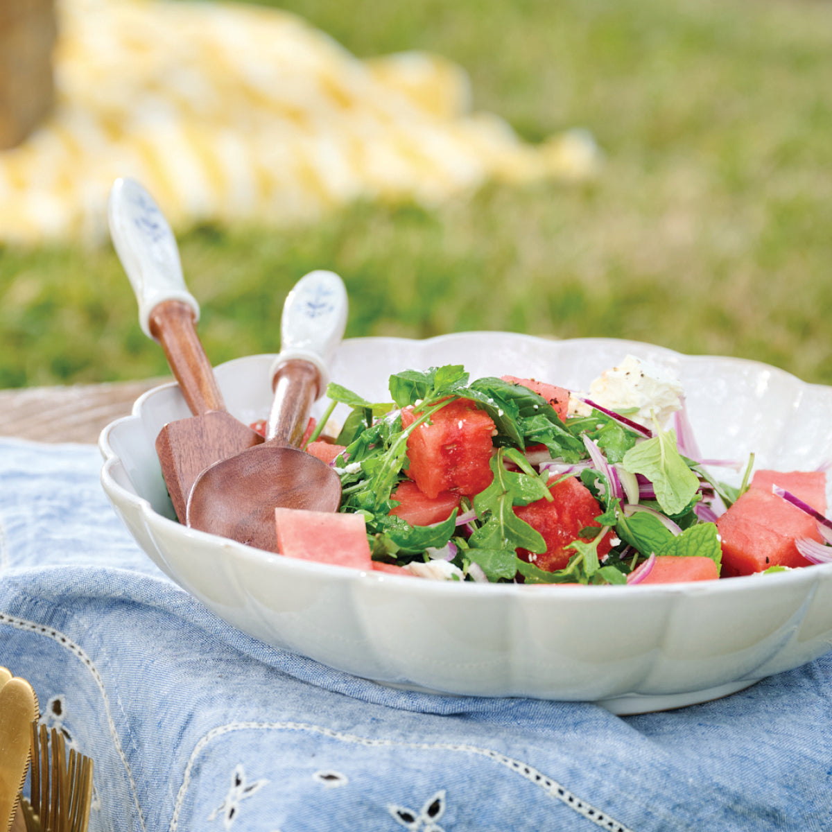 Watermelon & Feta Salad, ready to enjoy in a scalloped bowl with wooden tongs.