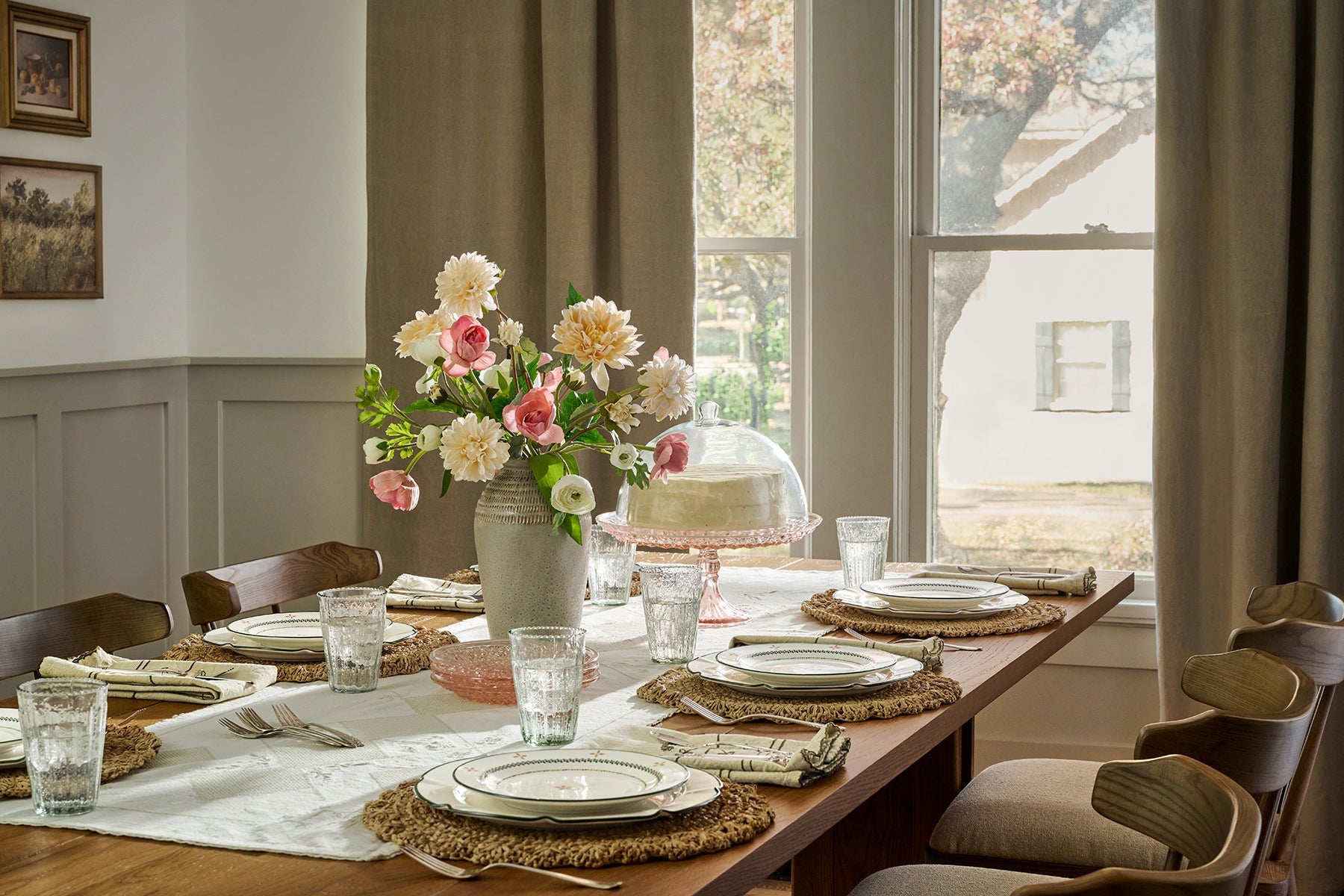 A white cake and a bouquet of pink and white flowers sit on a table set with Magnoliass dishes and glasses.