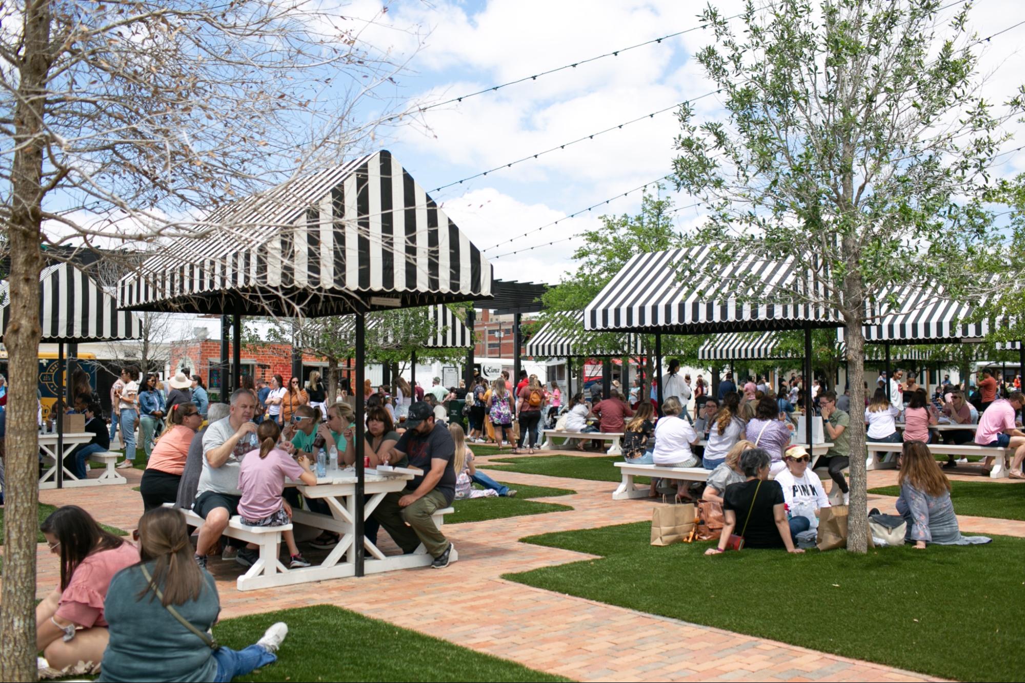 Outdoor food truck area at the Silos with people under striped canopies in a park-like setting.
