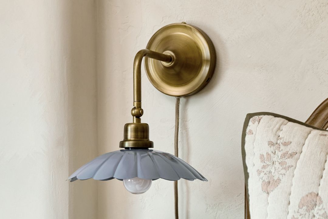 Plug in sconce hanging on wall. Black metal arm with scalloped cream enamel shade.