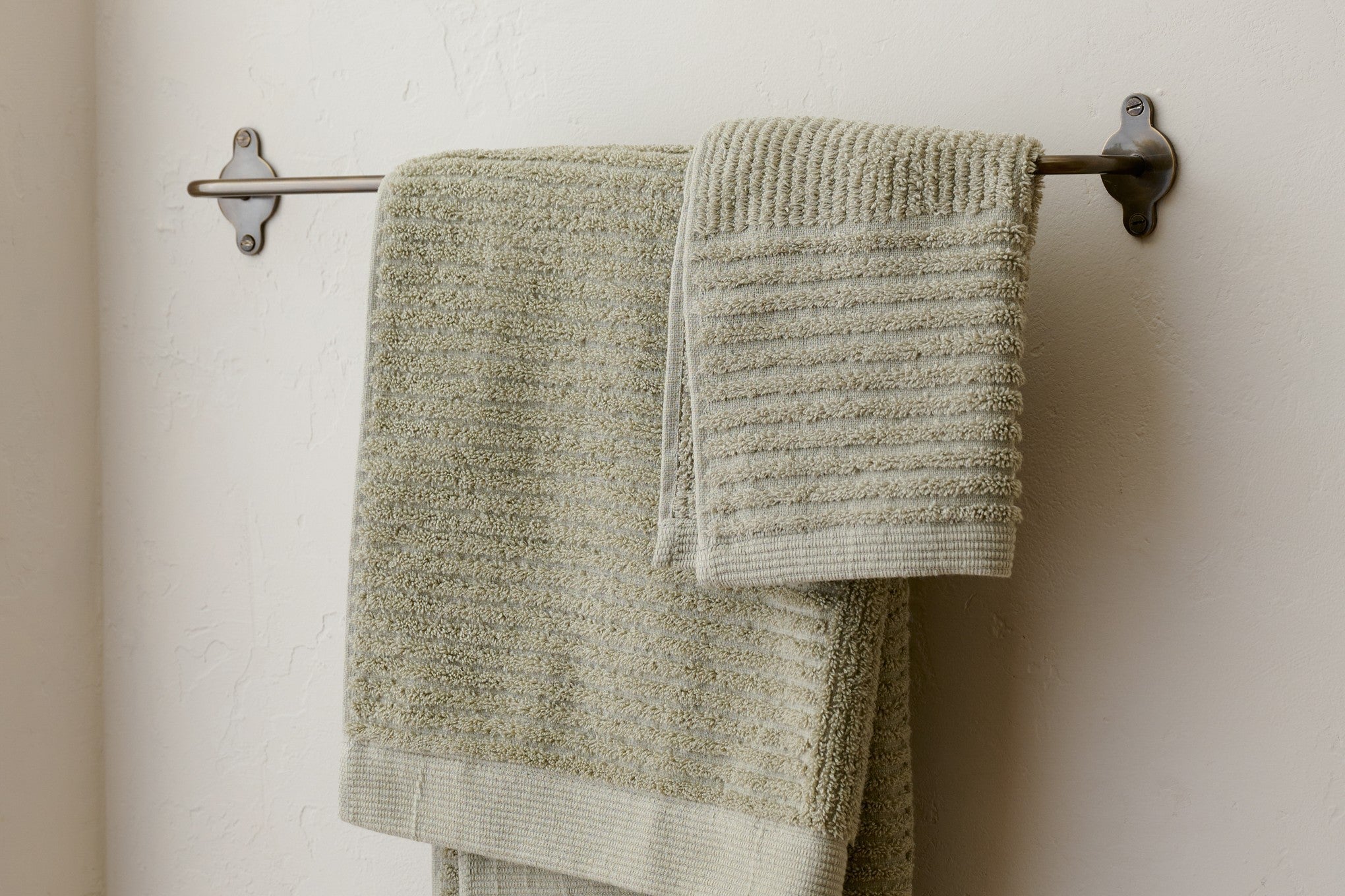 Shop bathroom towels and bath mats. Image features green bath towels hanging on towel rack.