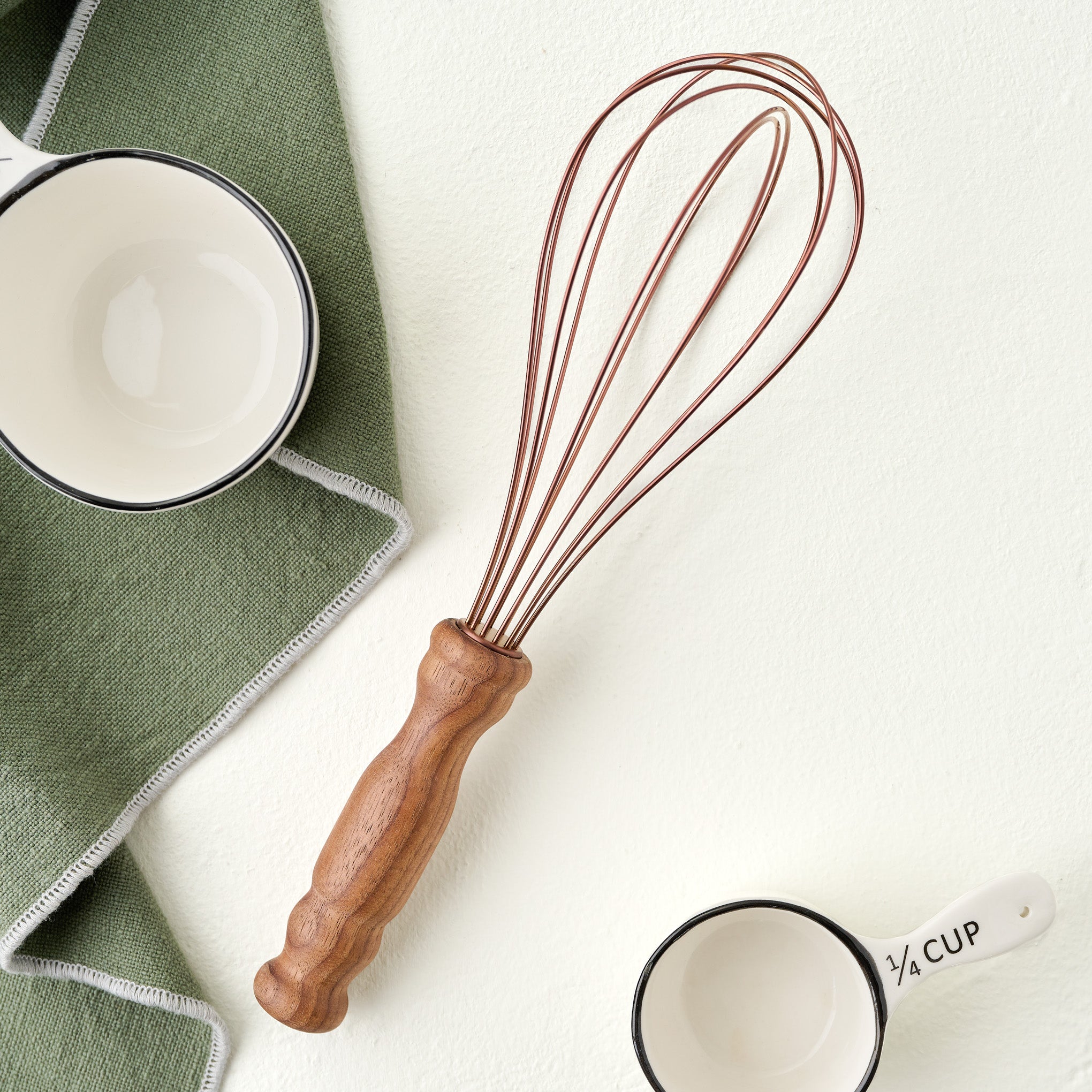 Copper and Walnut Whisk shown with measuring cups and kitchen towel