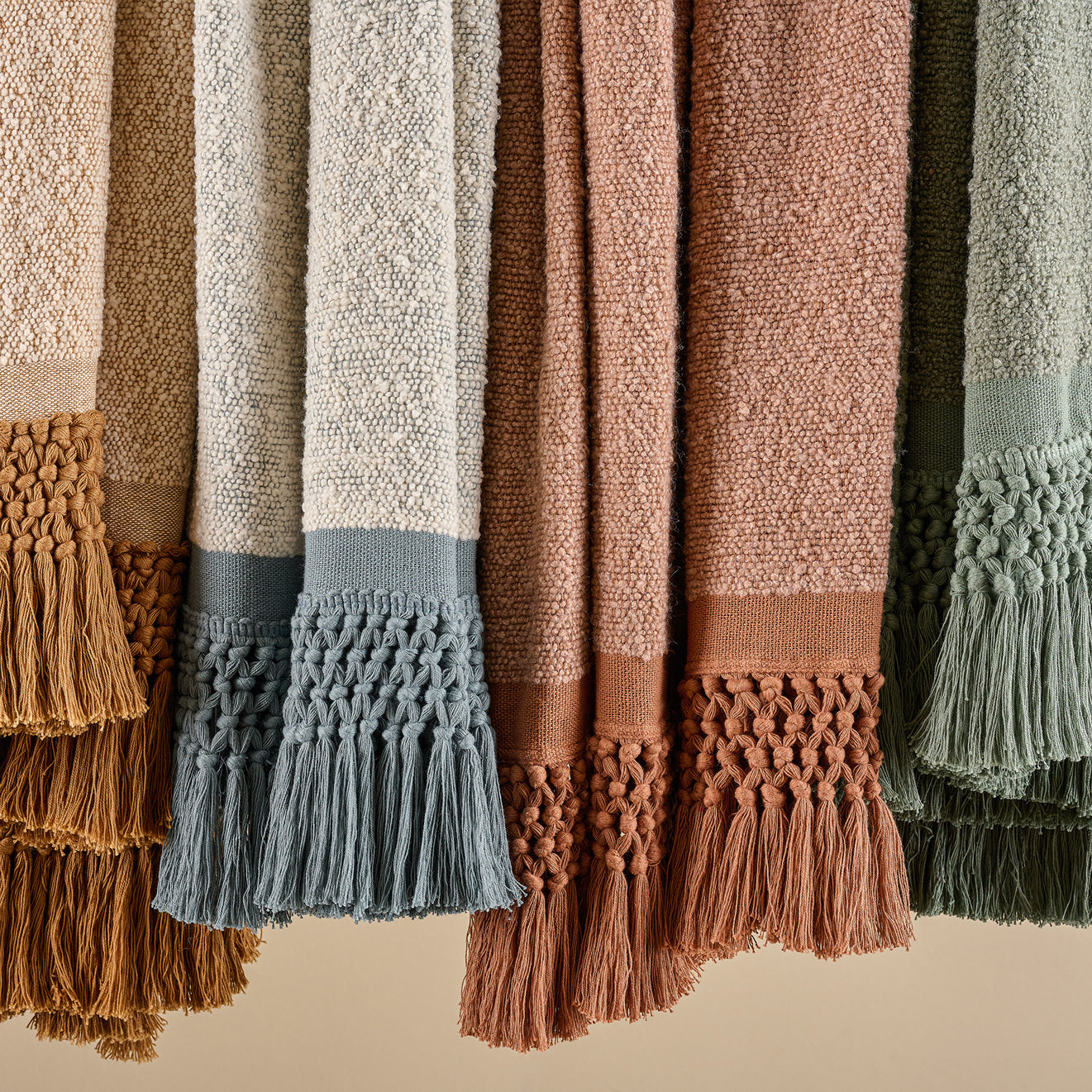 Collection of textured throw blankets with tassels in various colors on a beige background.  shop throw blankets.