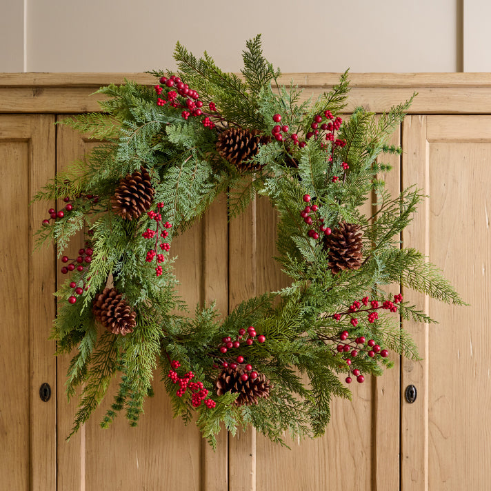 Christmas wreath with greenery, red berries, and pinecones on a wooden door.