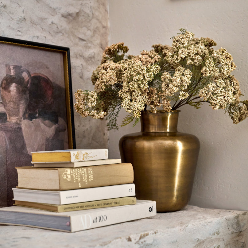 Decorative setup with books, a bronze vase, and flowers against a neutral wall.  Shop Decor.