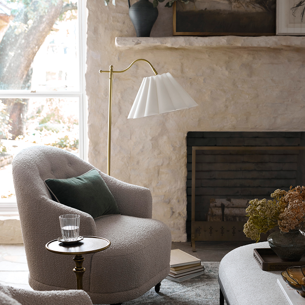 Cozy living room with a plush armchair, side table, and lamp near a fireplace.  Shop the Living Room.