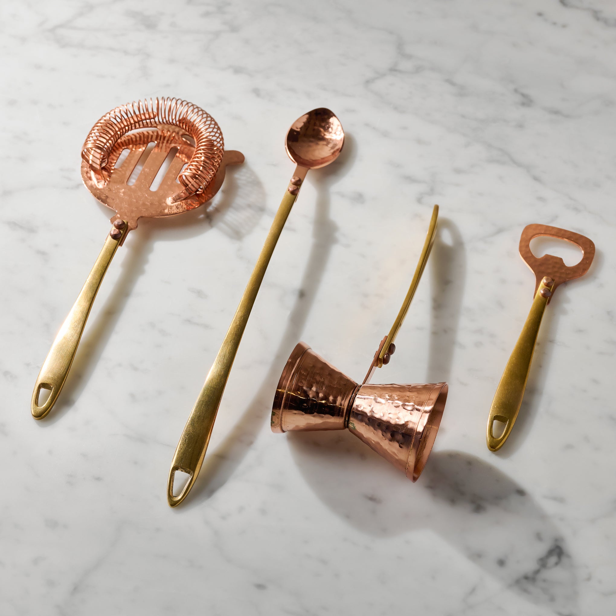 Hammered Copper and Gold Bottle Opener shown with other bar tools on marble counter