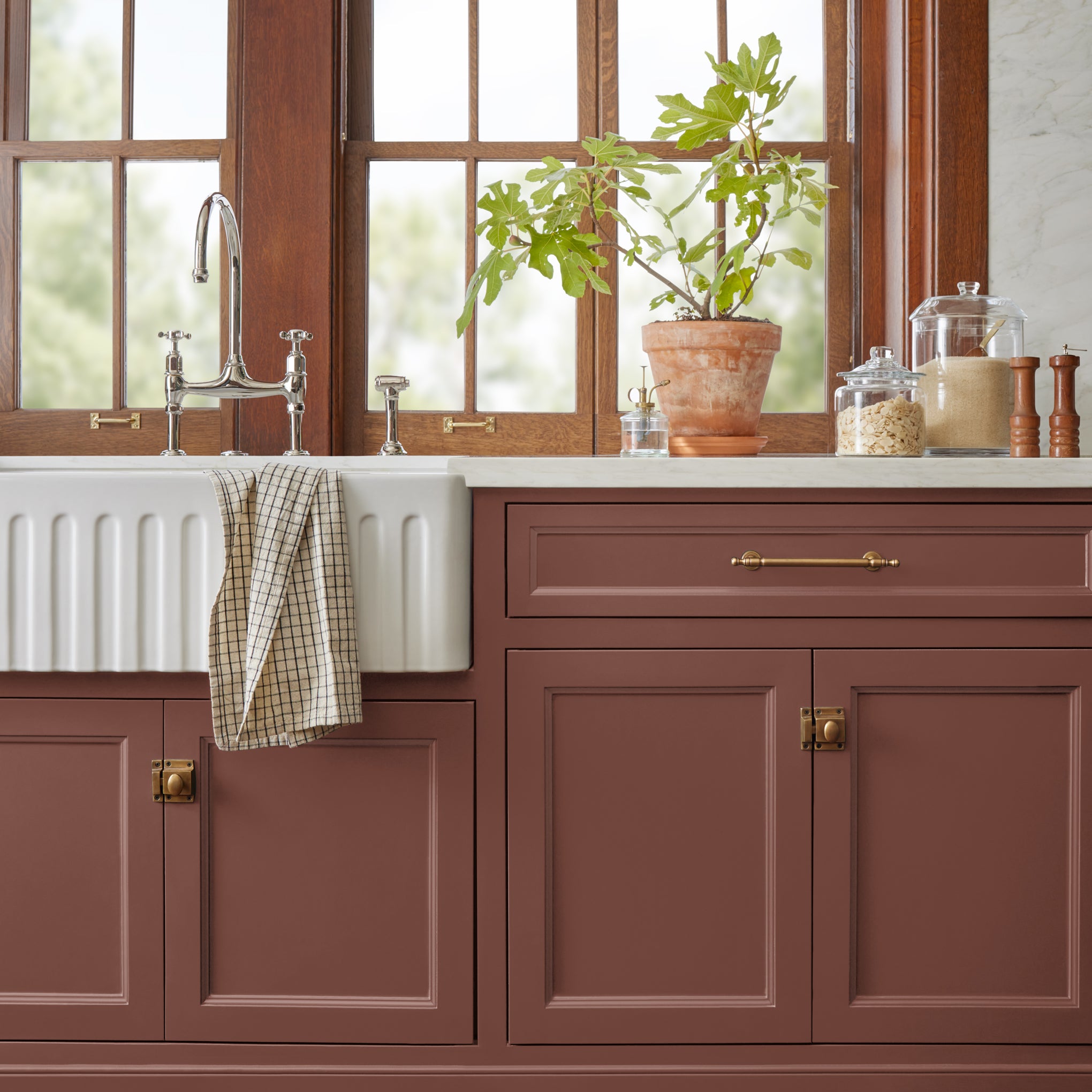 Mountain Currant paint featured on bottom kitchen cabinetry with white farmhouse sink, potted plant and glass kitchen jars