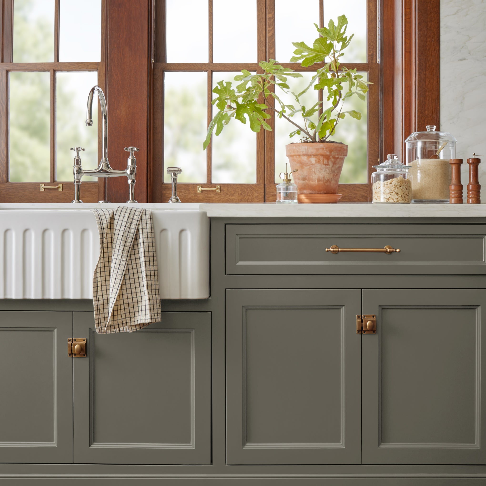 Trailhead paint featured on bottom kitchen cabinetry with white farmhouse sink, potted plant and glass kitchen jars