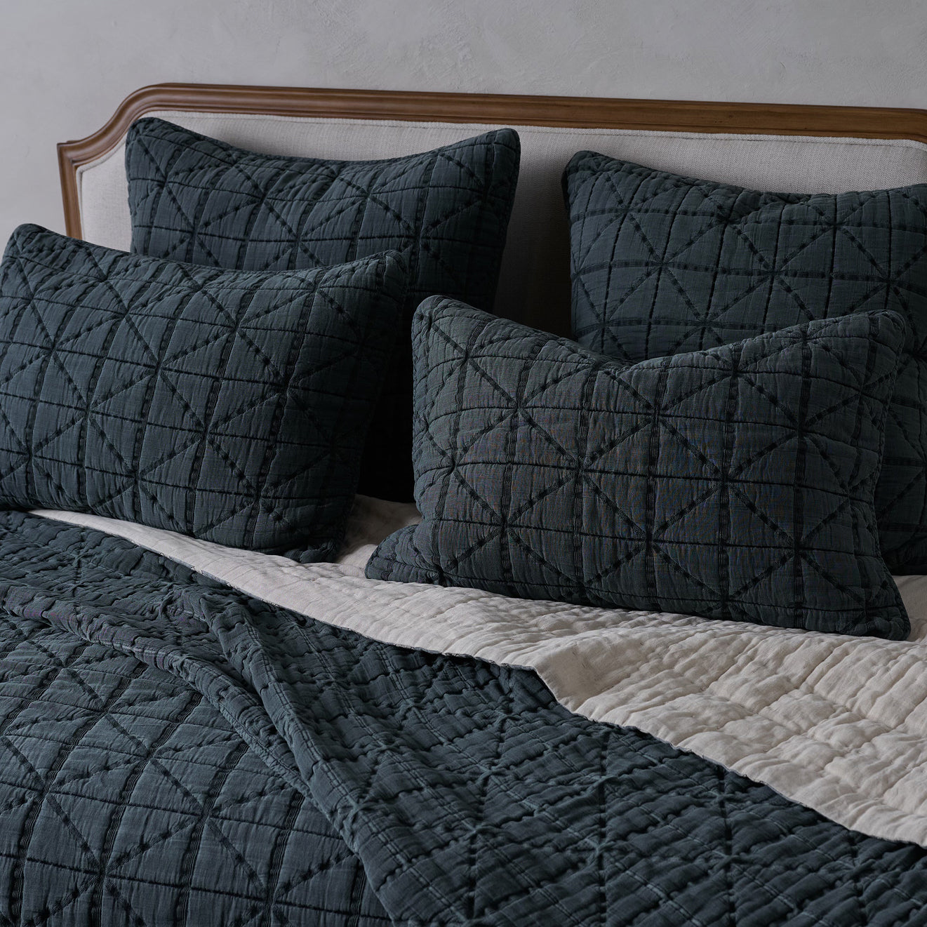 Bed with dark gray quilt and matching pillows on a neutral background
