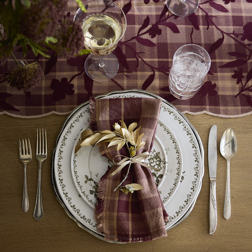 Dining table setting with plaid napkin, silverware, and glasses on a patterned tablecloth. Shop Kitchen + Dining.
