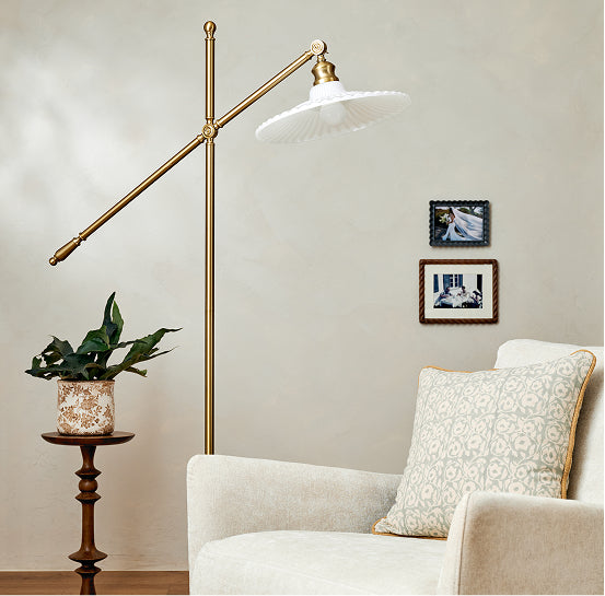 Floor lamp in a living room setting with a plant and framed pictures on the wall.