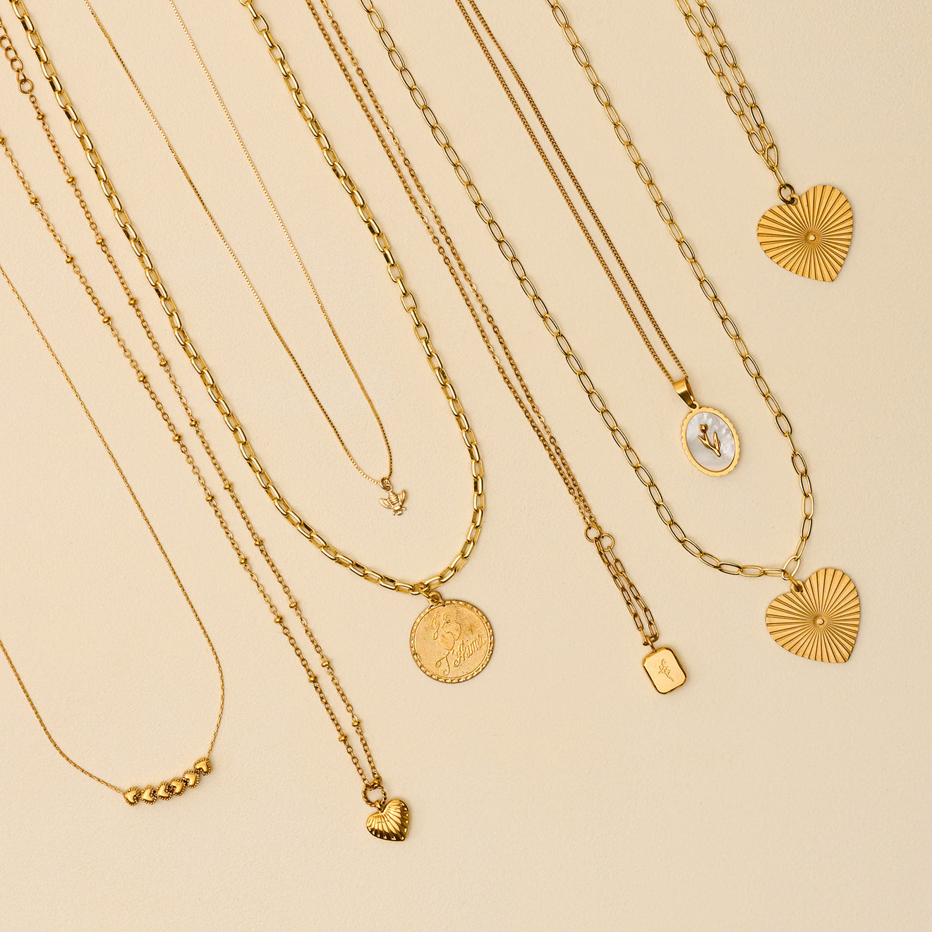 Collection of gold necklaces with various pendants on a beige background