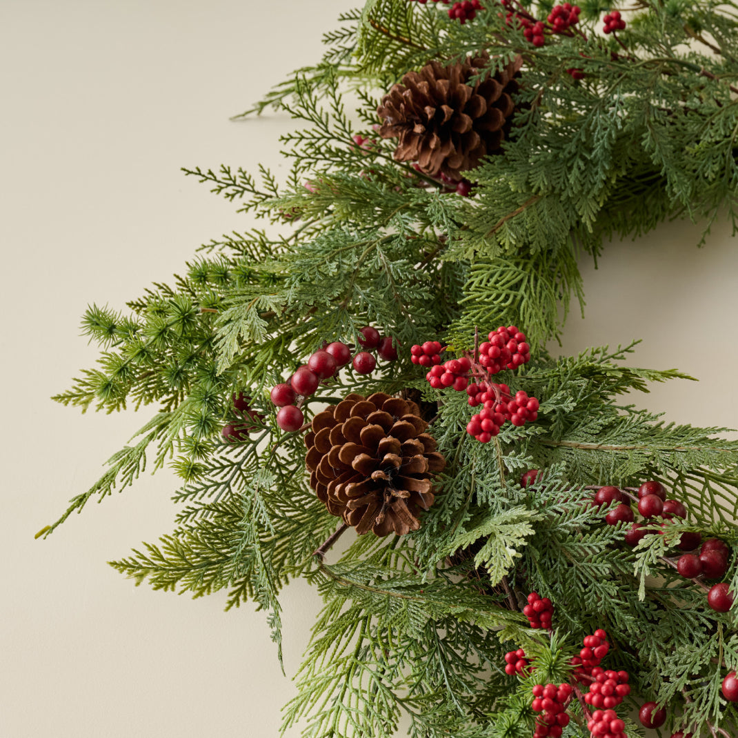 Christmas wreath with greenery, pinecones, and red berries on a neutral background