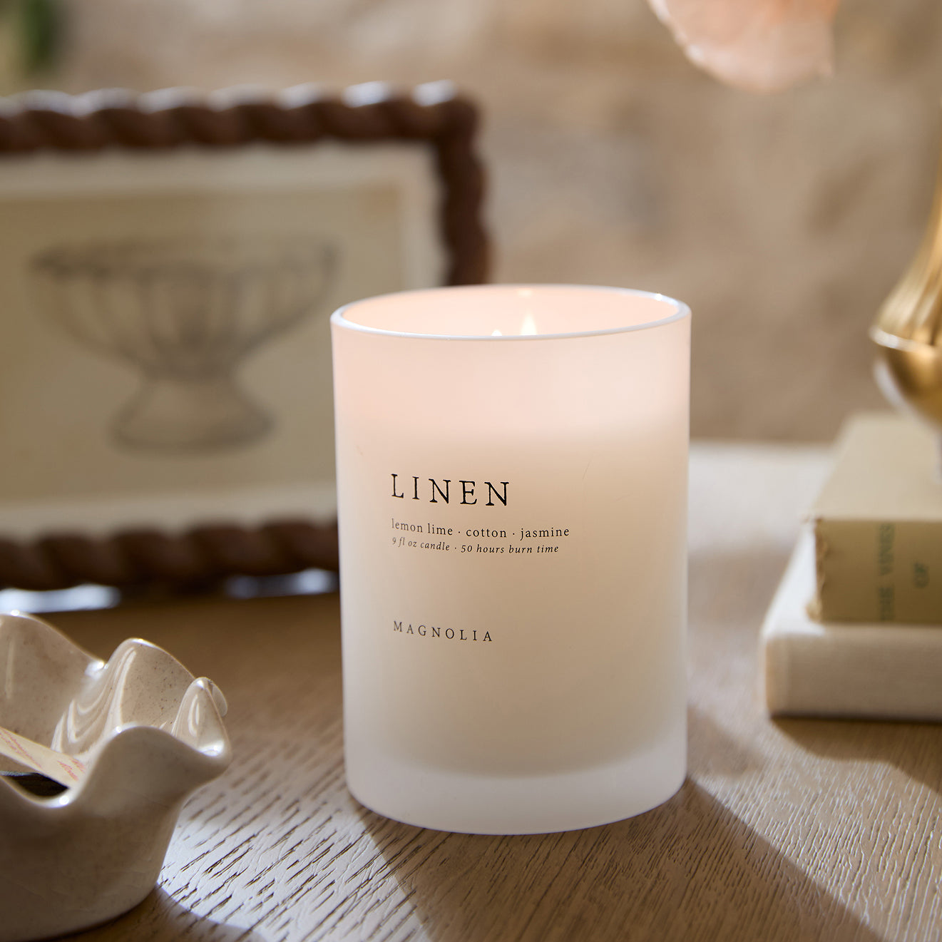 Candle labeled 'Linen' on a wooden surface with a blurred background.  shop candles.