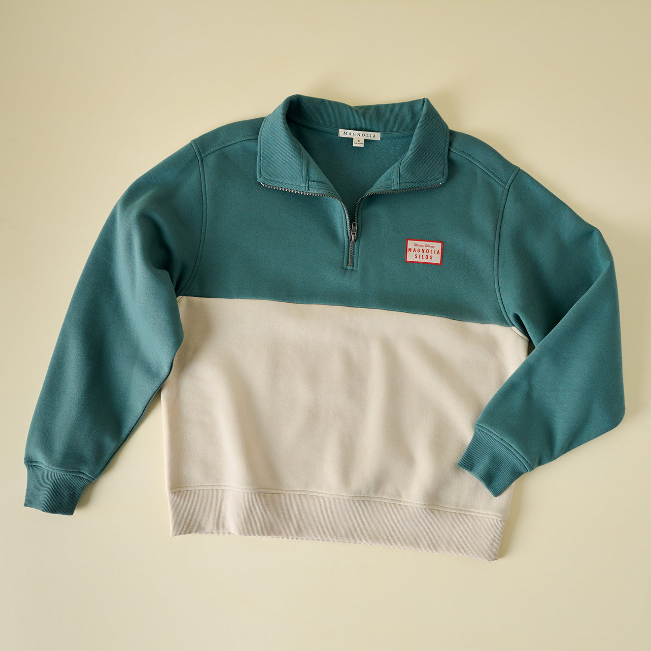 Two-tone teal and beige sweatshirt with a logo on a beige background