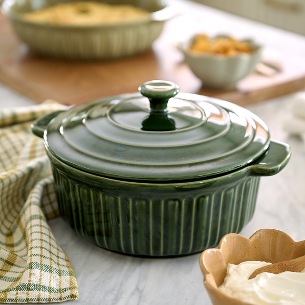 Green ceramic casserole dish with lid on a kitchen counter with a towel and small bowl of cream.  Shop the Kitchen.