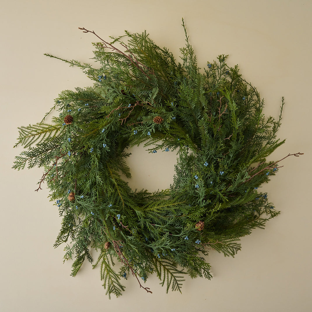 Green wreath with pine needles and small cones on a beige wall