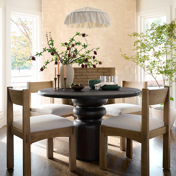 Dining room with a dark round table and wooden chairs with white cushions, decorated with flowers and candles.  Shop the Dining Room.
