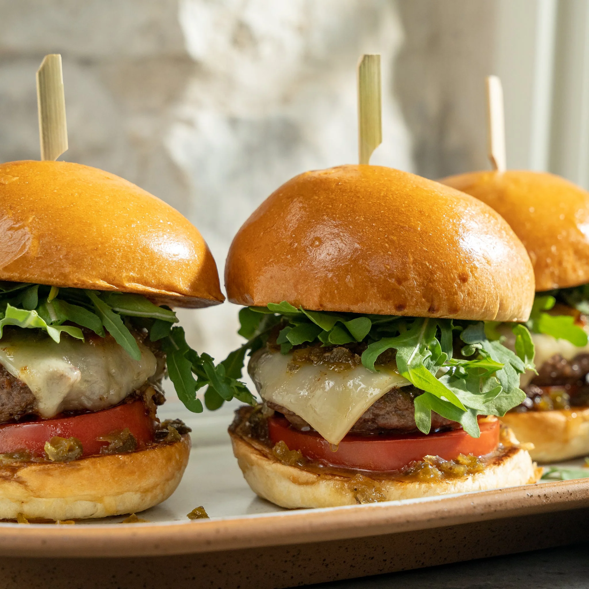 Three burgers with lettuce, tomato, and cheese on a plate with a blurred background