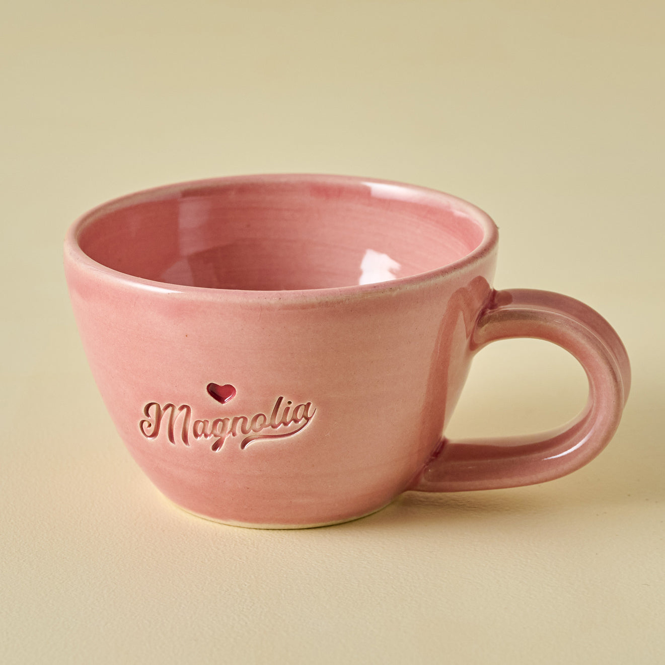 Pink mug with 'Magnolia' branding on a beige background.  shop coffee mugs.