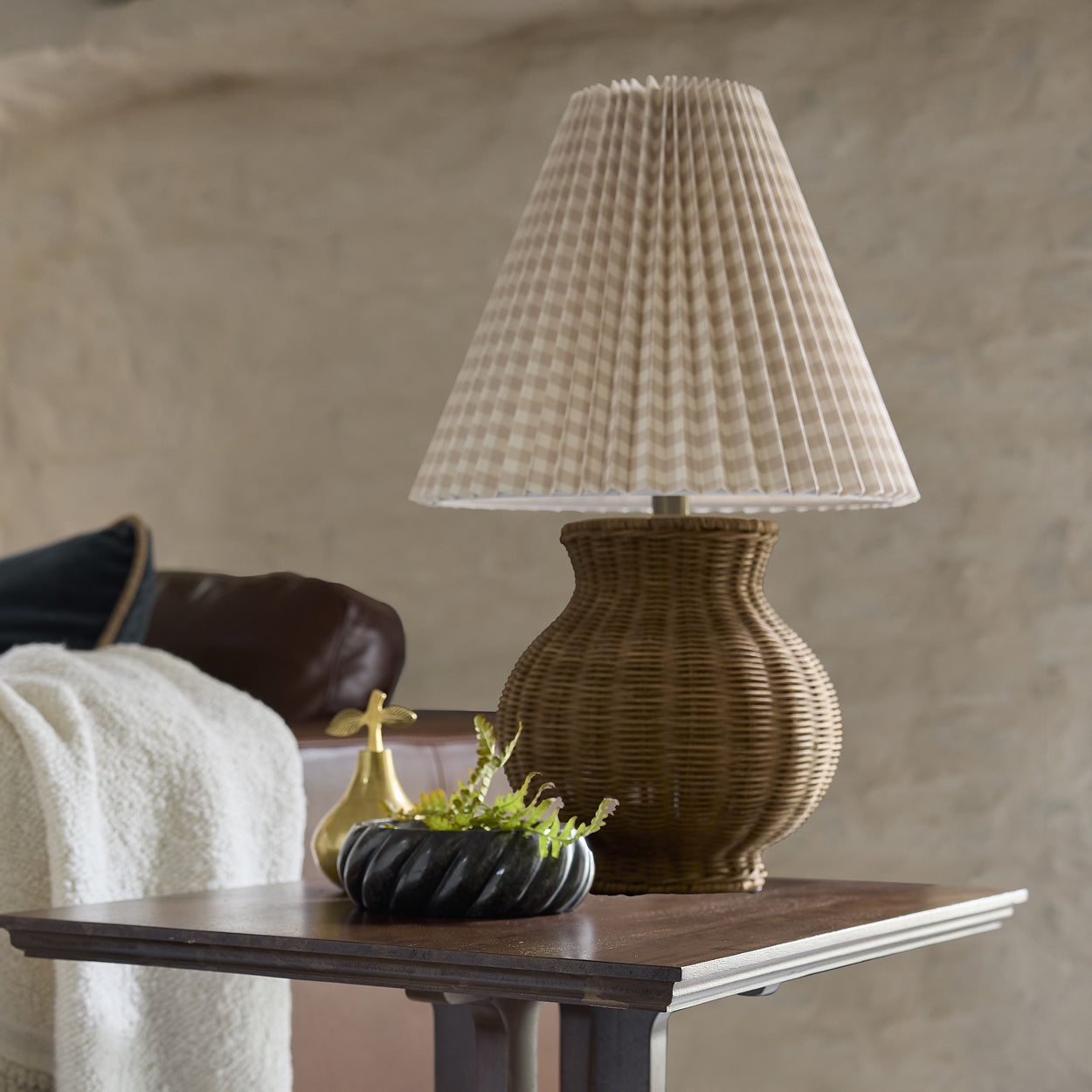 Wicker table lamp on a wooden side table with decorative items against a neutral wall.  Shop lighting.