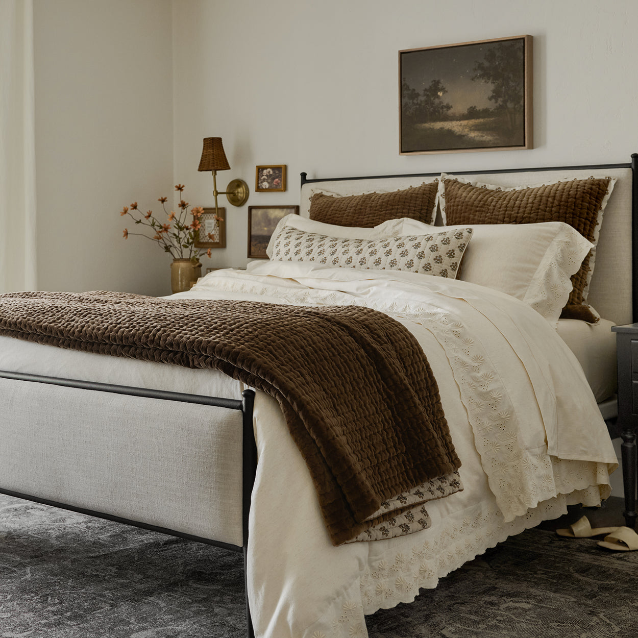 Neatly made bed with decorative pillows and a blanket in a bedroom setting.  Shop Bedding.