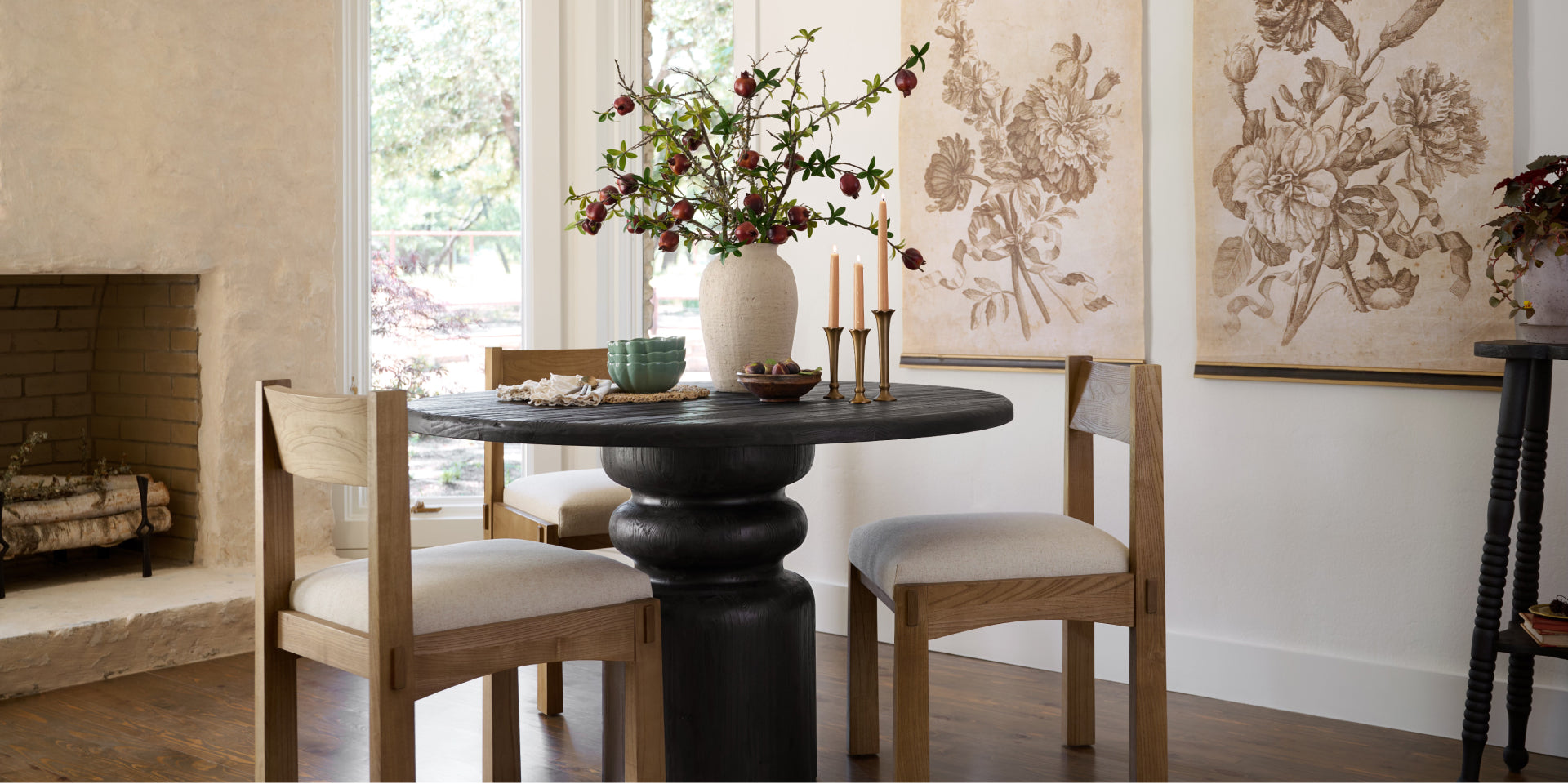Dining room with a round black table and wooden chairs, featuring a vase of flowers and framed artwork.  Shop New Arrivals.
