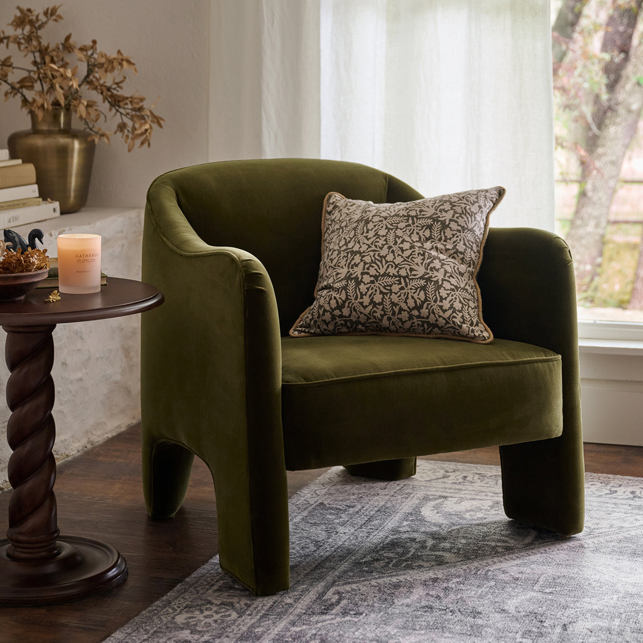 Green armchair with a patterned pillow in a room with a side table and window.  Shop Furniture.