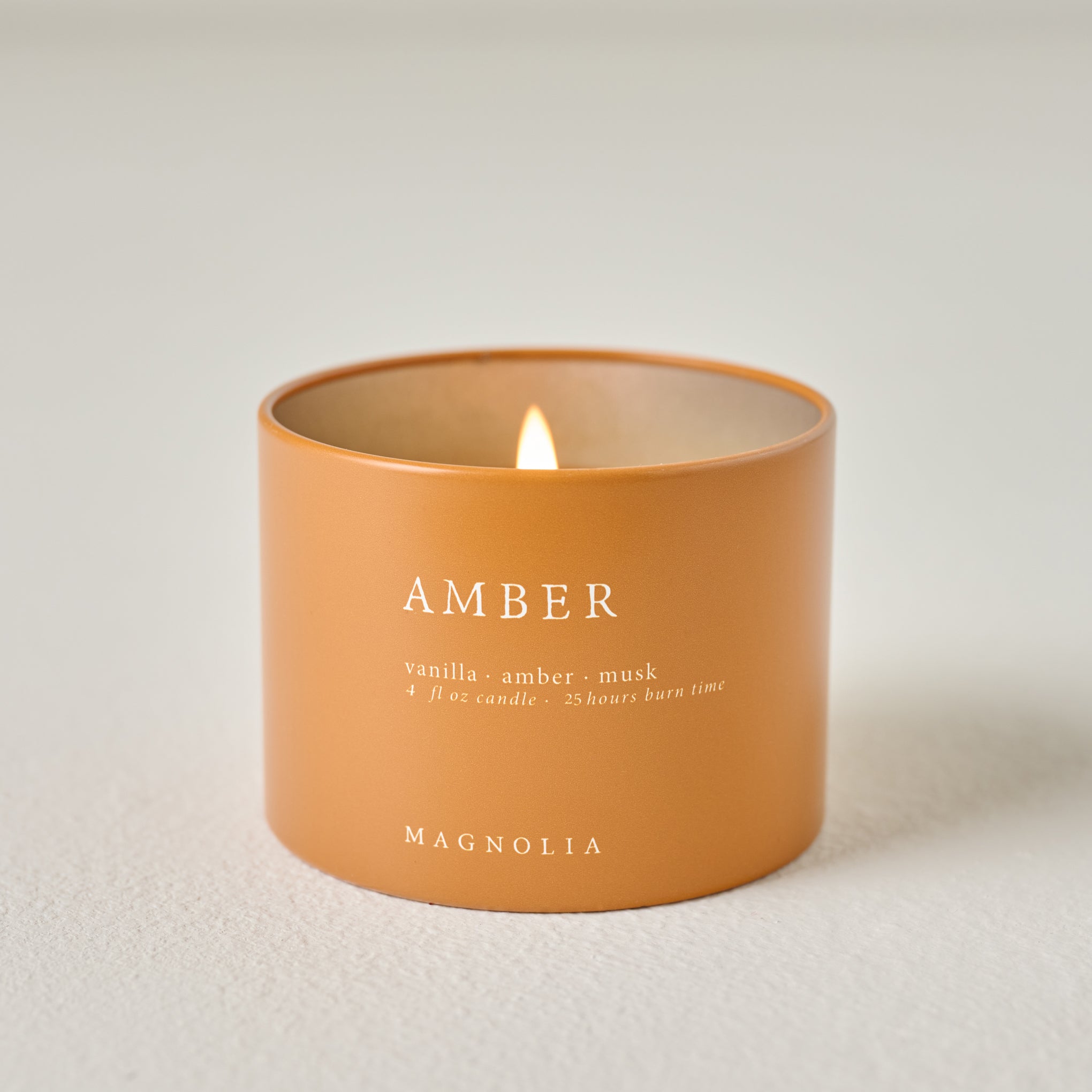 Magnoliass Amber Candle Tin shown burning