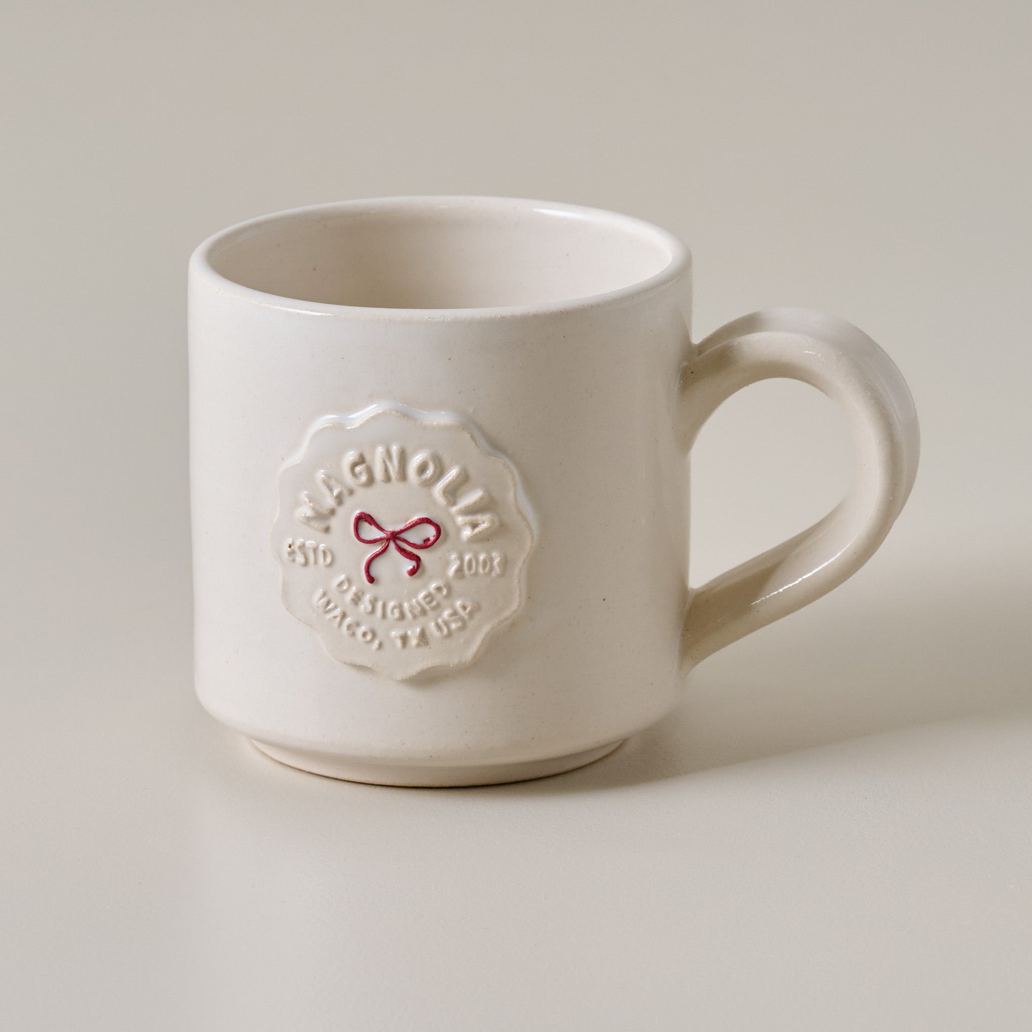 White mug with Magnoliass logo and red bow on a light background