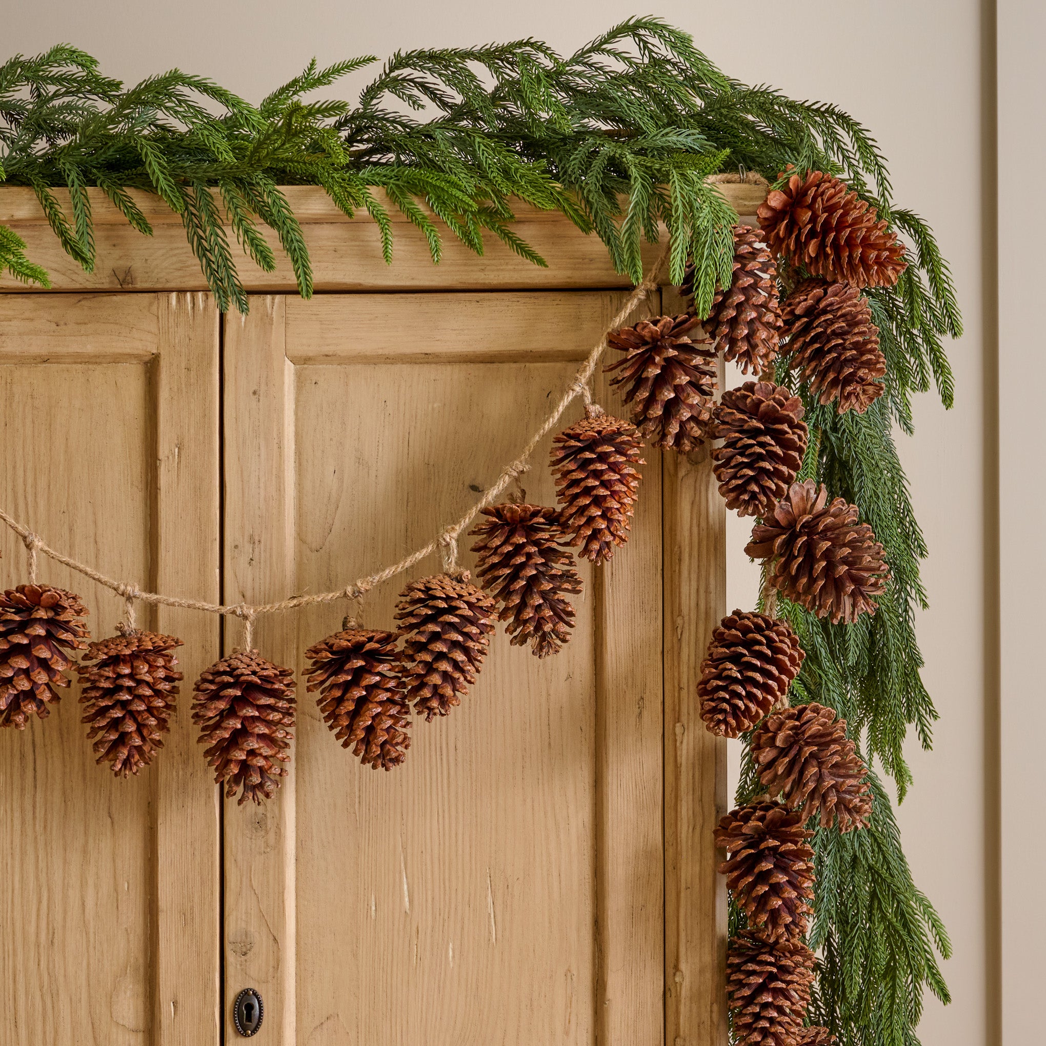 Natural Pinecone Garland shown hung on cabinet with greenery