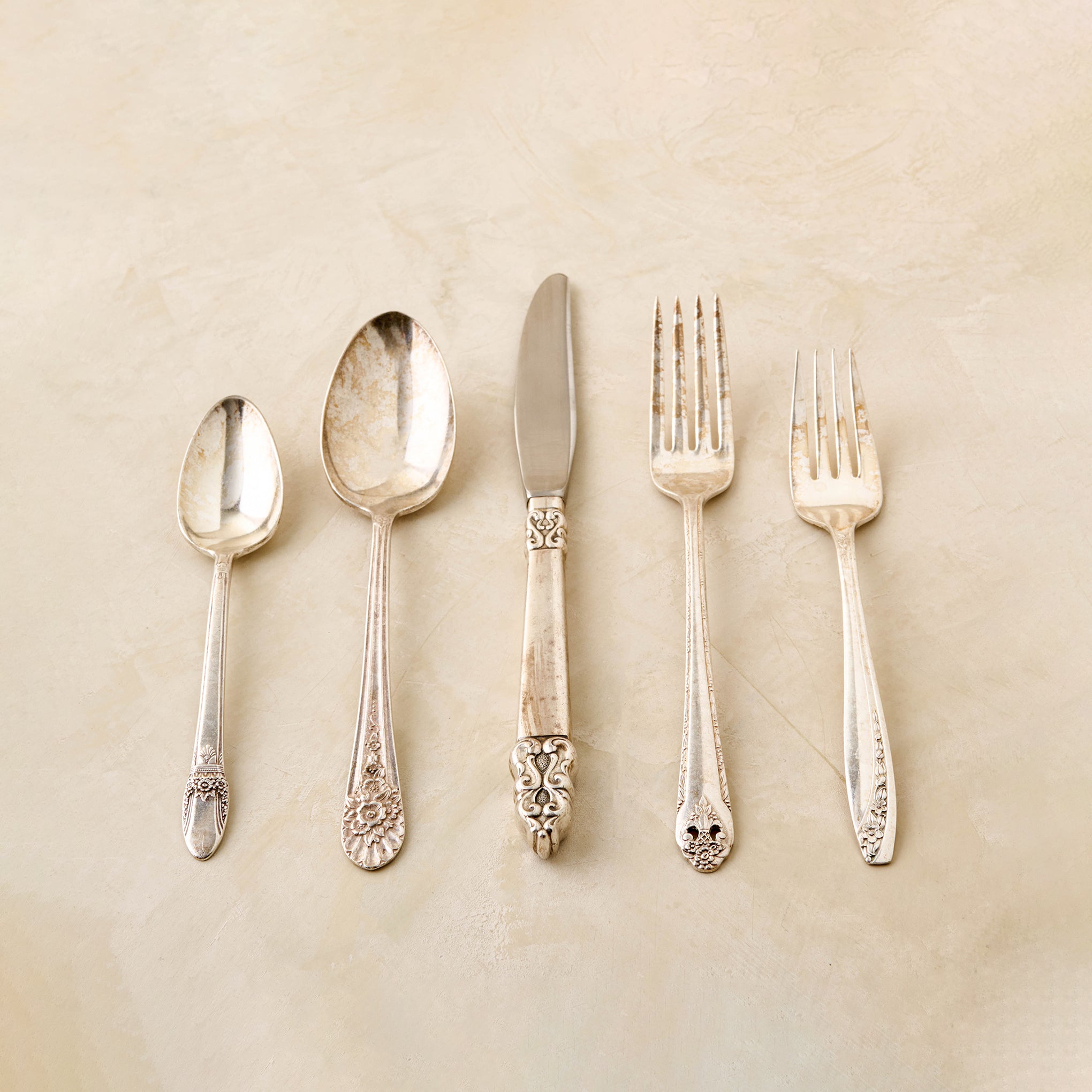 Set of silverware including spoons, a knife, and forks on a beige background