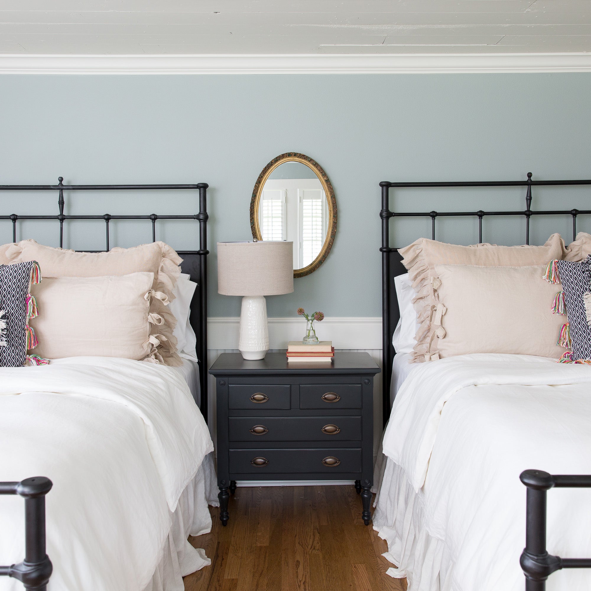 Two beds with black metal frames and white bedding in a bedroom with a nightstand and mirror.