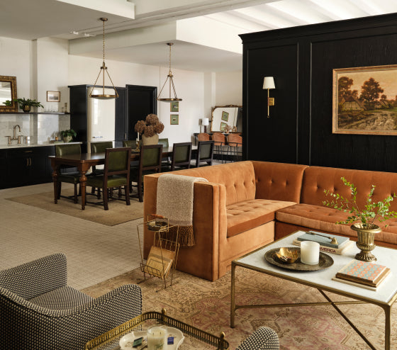 A hotel room at Hotel 1928 featuring a living room area with brown sectional sofa, coffee table, and dining area.