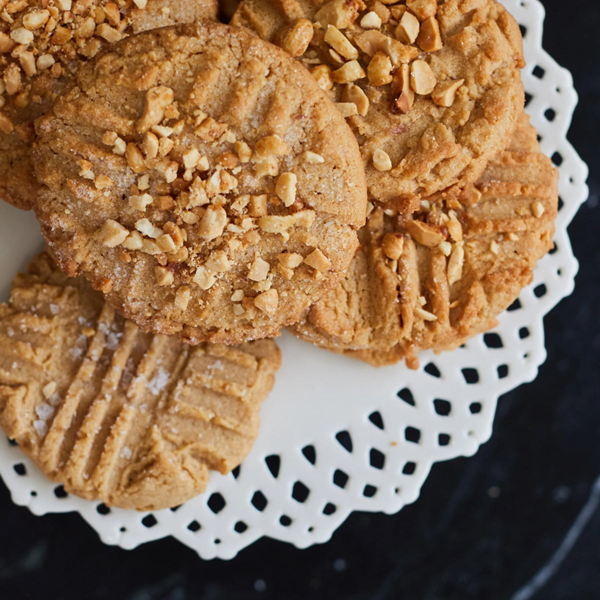 Peanut butter cookies with chopped nuts on a white doily.