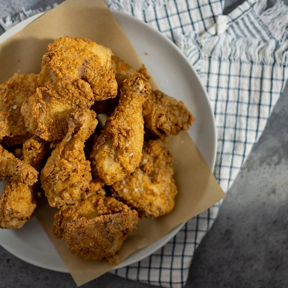 Fried chicken on a white plate with a checkered cloth in the background.