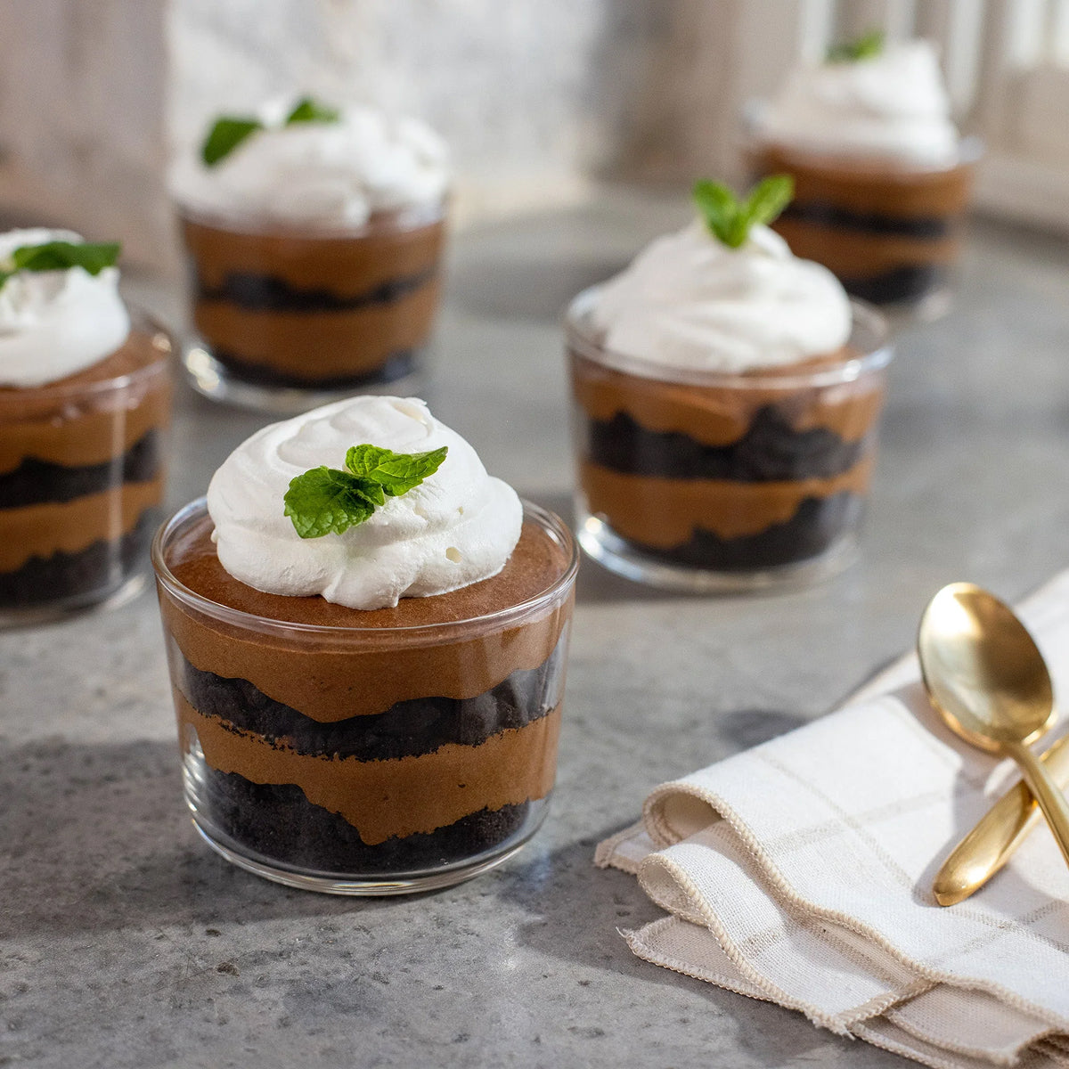 Small mocha trifle dessert cups with layers of chocolate, cream, and mint leaves on a gray surface.