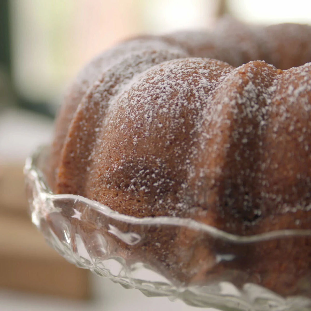 Pecan Bundt Cake with powdered sugar on a glass cake stand.