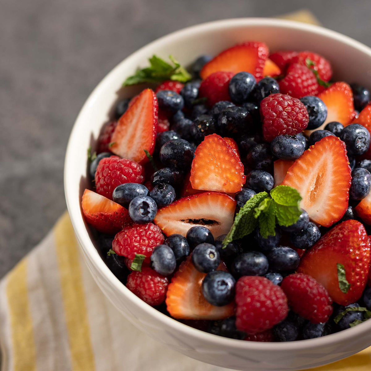 Bowl of mixed berries including strawberries, blueberries, and raspberries on a gray background.