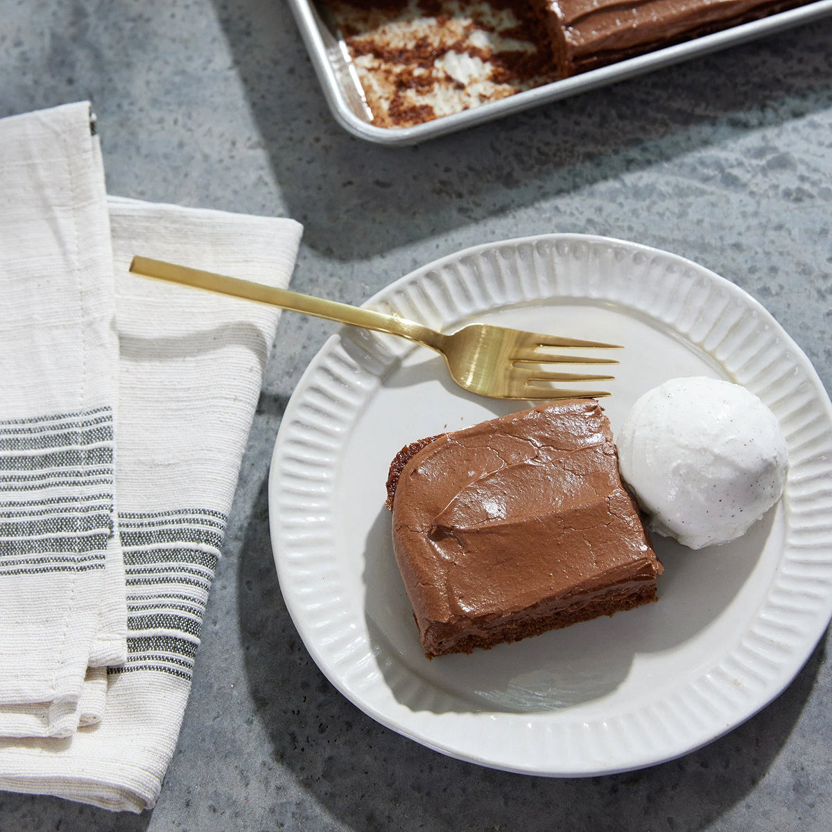 Chocolate-Cola Cake with Chocolate-Cola Buttercream on a white plate with a gold fork, on a gray surface.