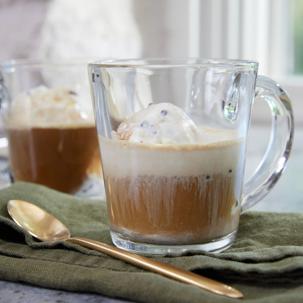 Clear glass mug with a layered drink (Affogato) and ice cream on a green napkin with a spoon.