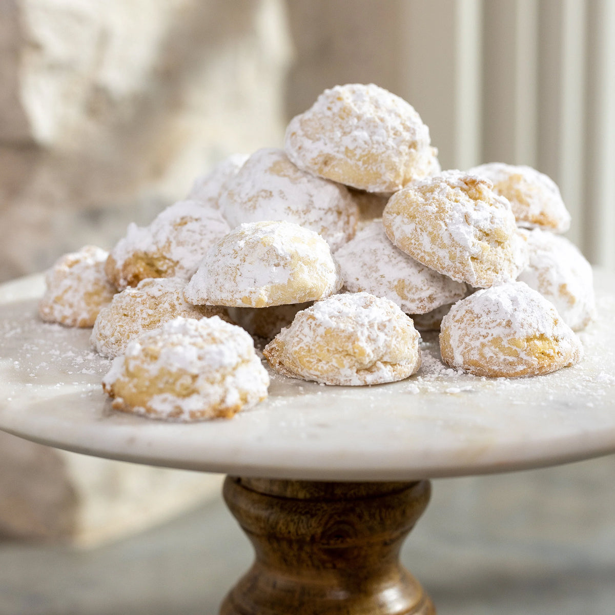 White powdered lemon tea cookies on a marble cake stand with a blurred background.