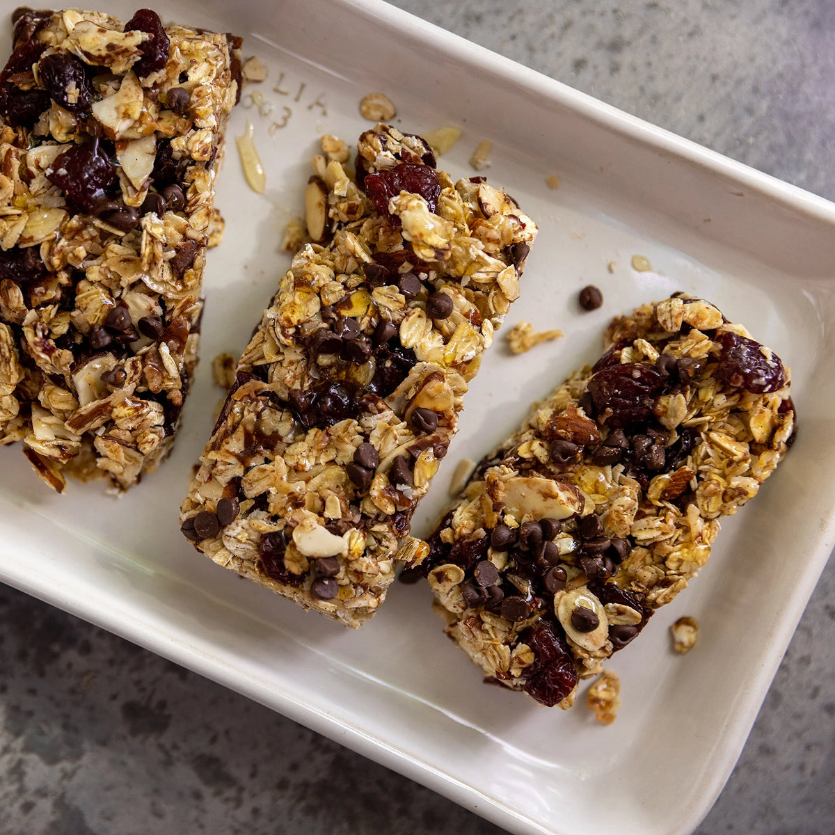 Three granola bars with chocolate chips, oatmeal, nuts and raisins on a white plate.