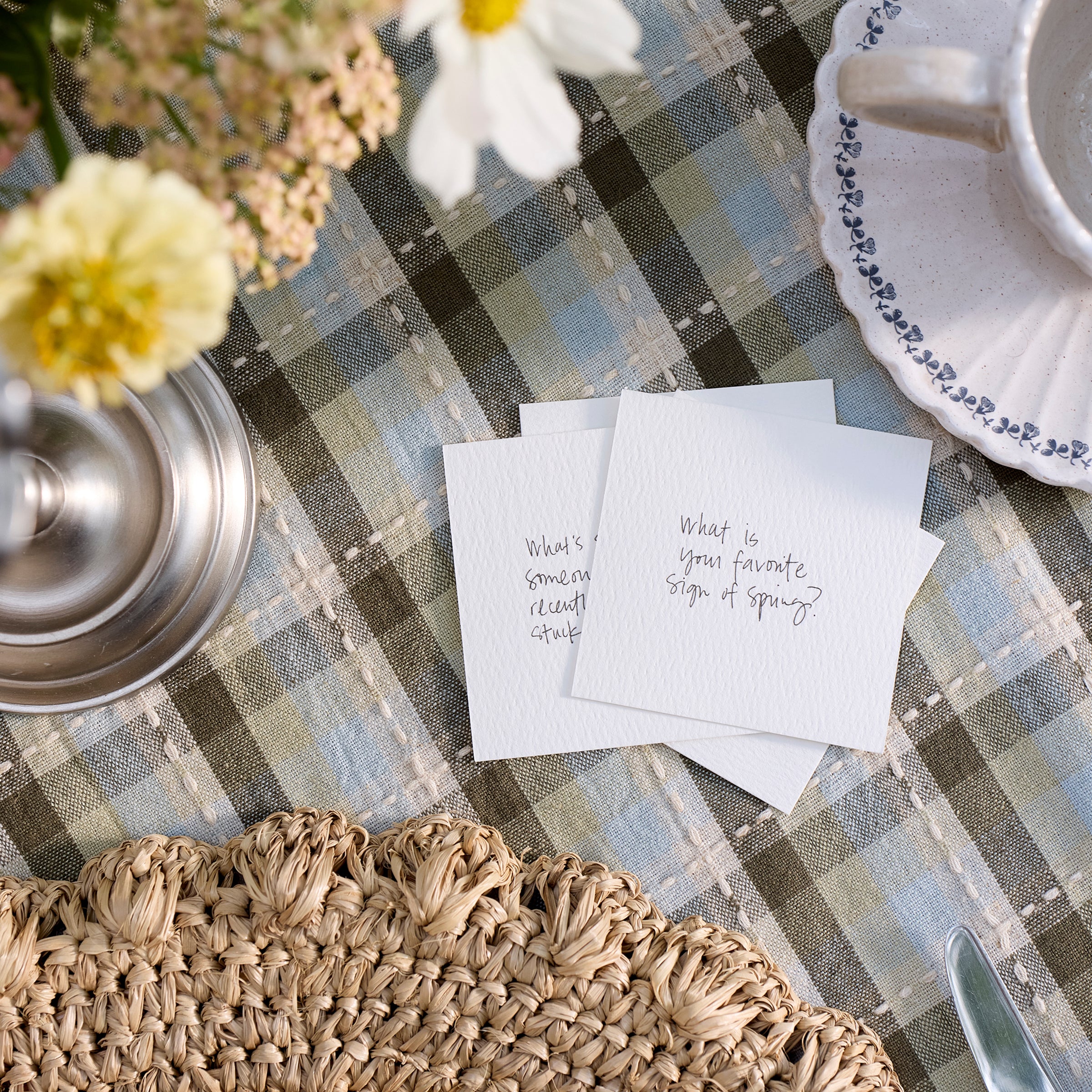 Table setting with plaid tablecloth, flowers, and cards on a checkered tablecloth.