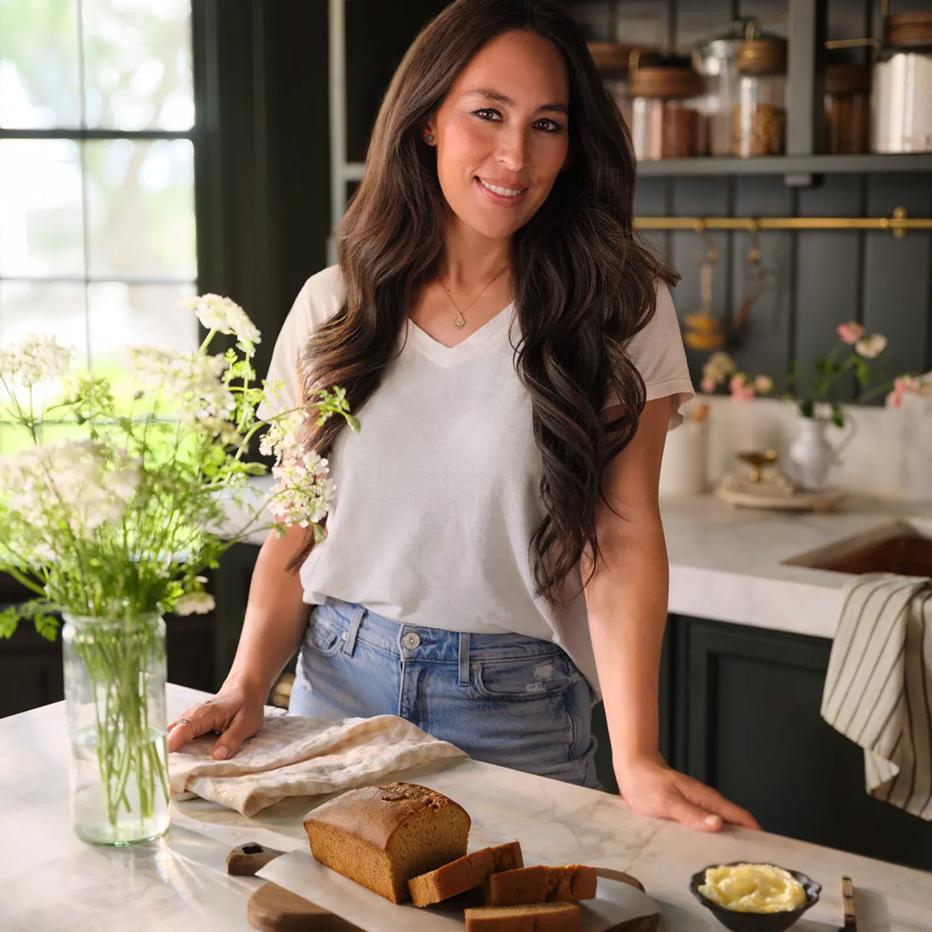 Joanna Gaines standing in her butler's pantry with a loaf of Magnoliass Table After School Banana Bread on the kitchen island.