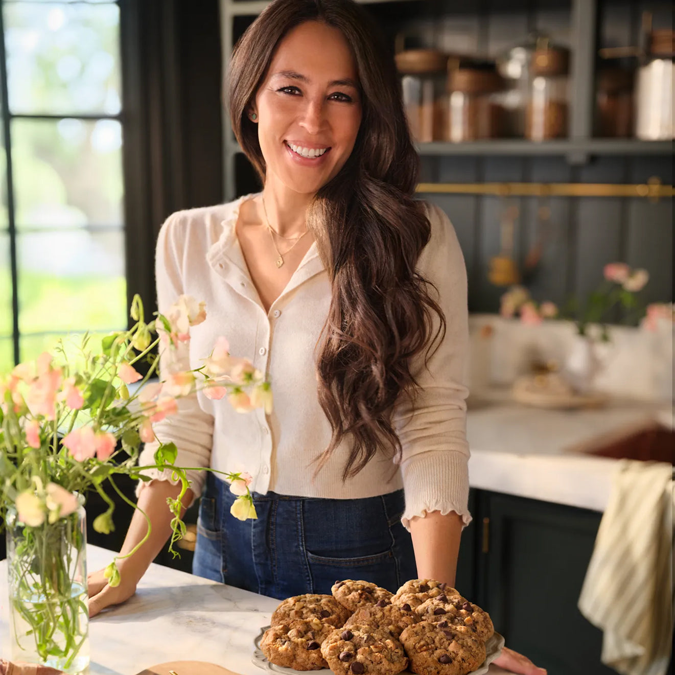 Joanna Gaines standing in her butler's pantry with vase of flowers and a cake plate full of Magnoliass Table Silo Cookies.